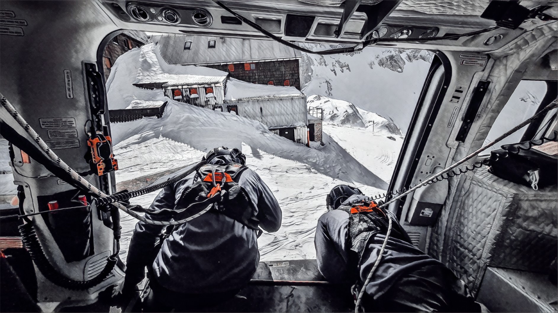 Gorska reševalca se nagibata iz policijskega helikopterja v gorah pozimi, pogled iz kabine
