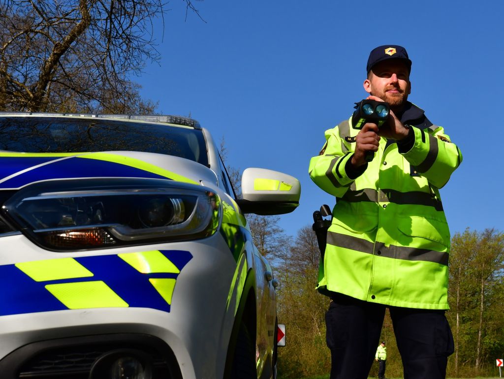 prometni policist ob policijskem belo-modro-rumenem patruljenem vozilu meri hitrost z ročnim radarjem_foto PU Novo mesto