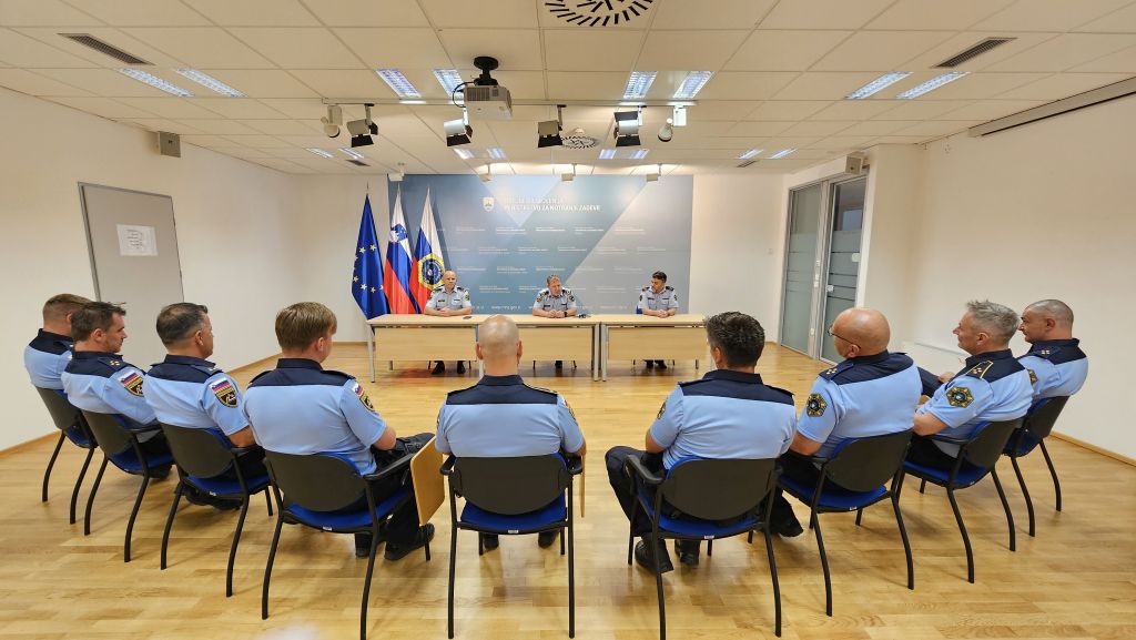 Devet policistov, sedi v polkrogu pred namestnikom generalnega direktorja policije