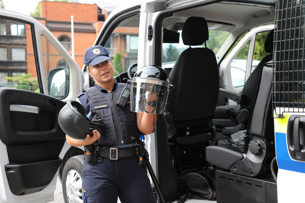 Policistka zbranim kaže policijske čelade in razlaga, kje se uporabljajo.