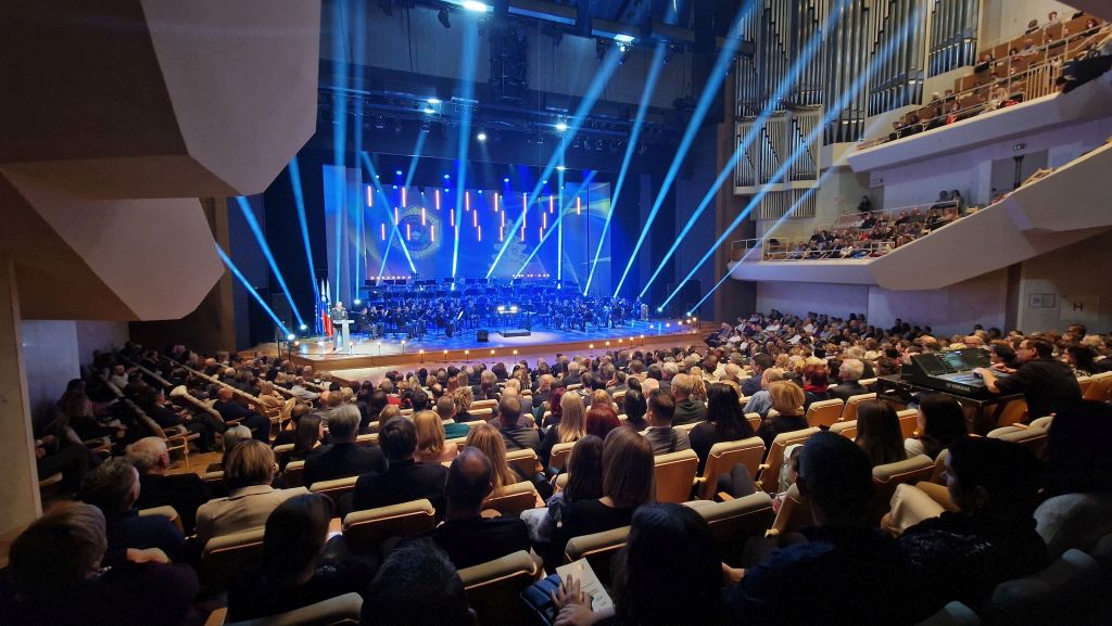 Polna Linhartova dvorana v Cankarjevem domu, na odru, ki ga osvetljujejo snopi modre luči, igra Policijski orkester