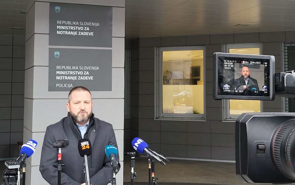 Primož Ogrinc med izjavo novinarjem (stoji zunaj pred vhodom v stavbo, pred njim so mikrofoni in kamere, v ozadju tabla z napisom MNZ Policija)