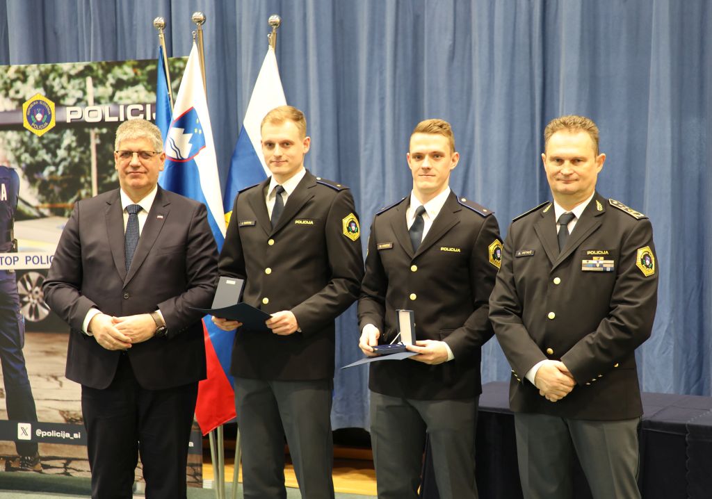 Prejemnika policista Matjaž Vrečič in Jure Ogrin na odru, v rokah imata medalji, ob njiju sta minister in v. d. generalnega direktorja policije