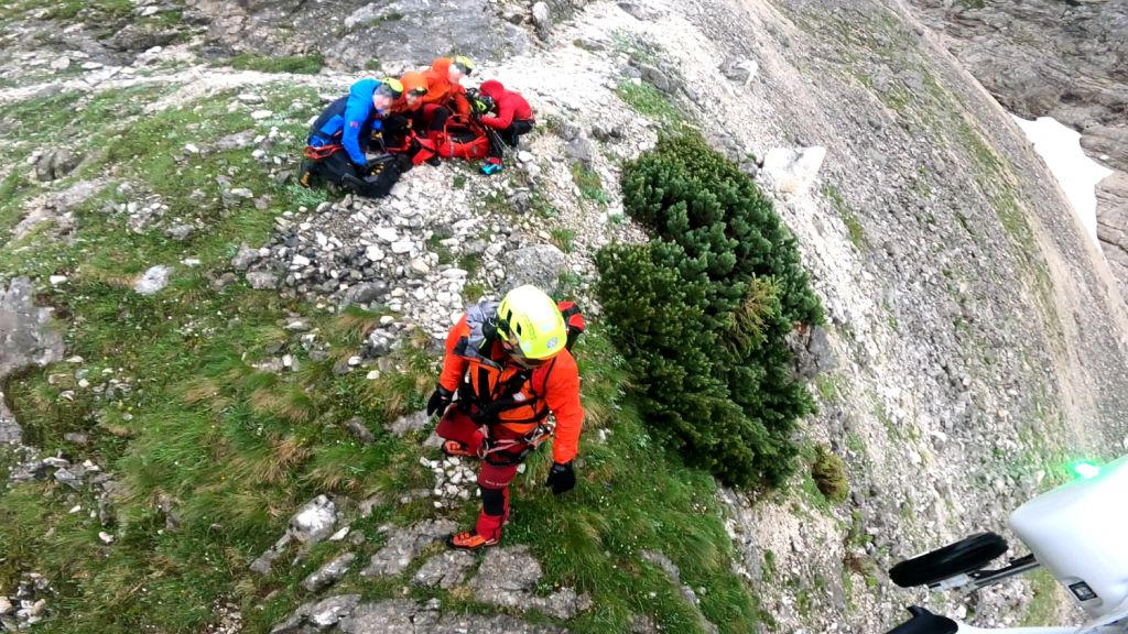 Reševanje na melišču - gorski reševalci oskrbujejov rdečih uniformah oskrbujejo ponesrečenca in nalagajo v vrečo za prevos s helikopterjem.