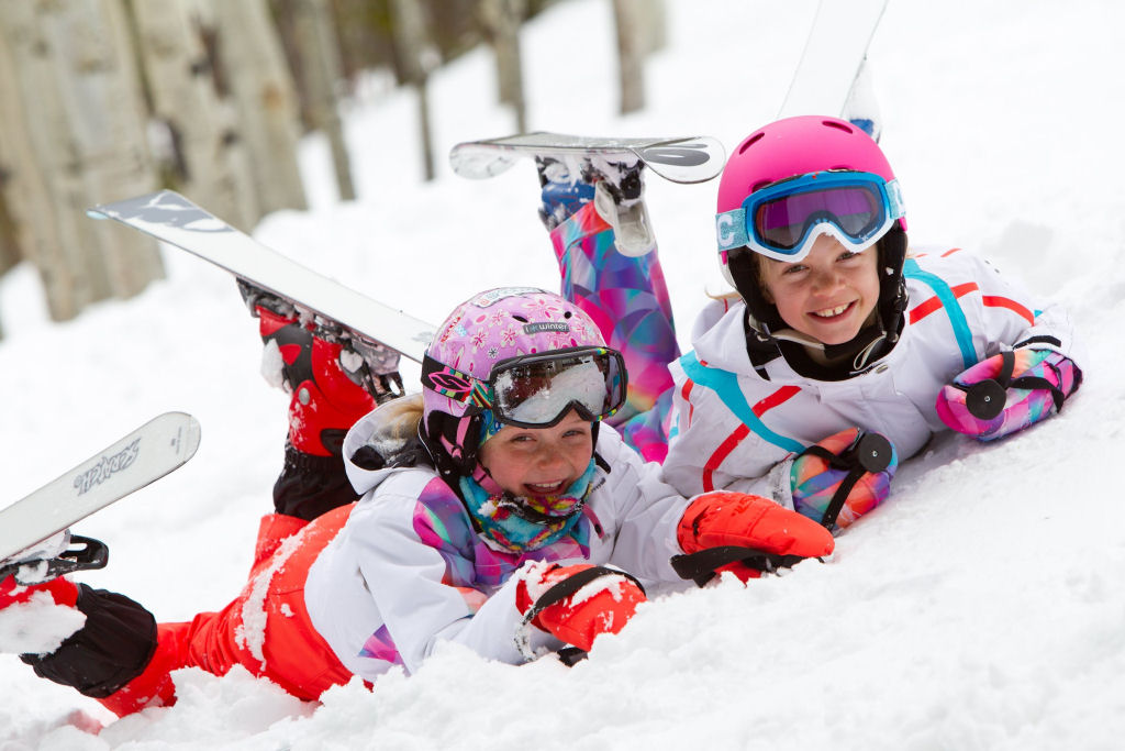 picture of two kids lying in the snow in ski equipment